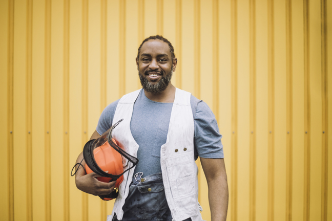 En glad man med en skyddshjälm under armen ler mot kameran.