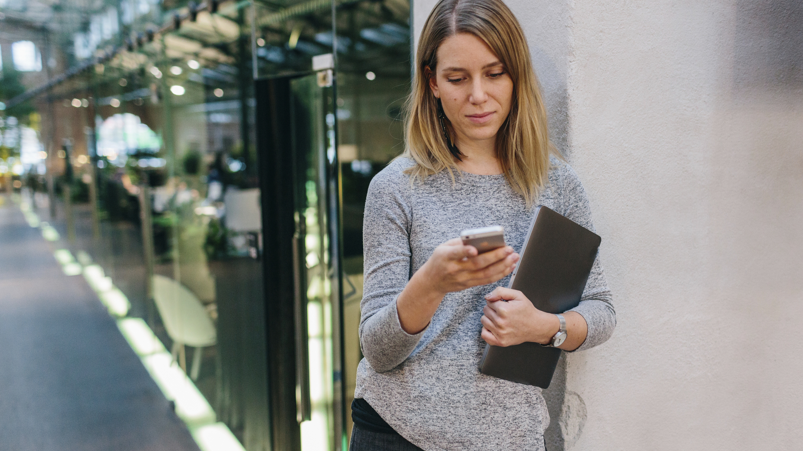 Kvinna på kontor lutar sig mot vägg tittar på telefonen